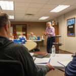 Man speaking to a group of other men gathered around the table