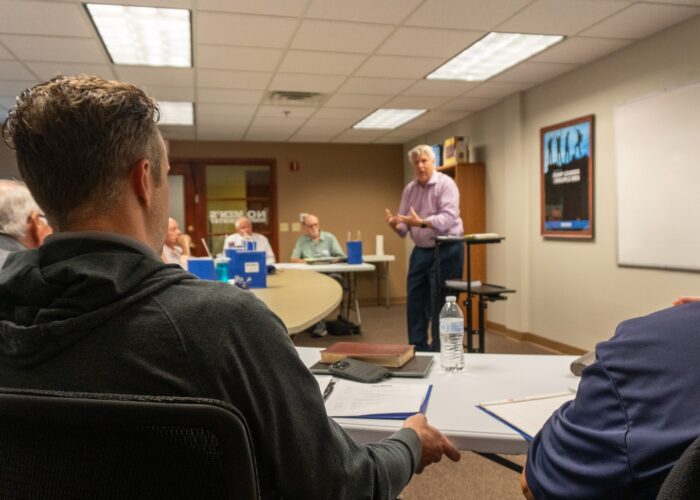 Man speaking to a group of other men gathered around the table