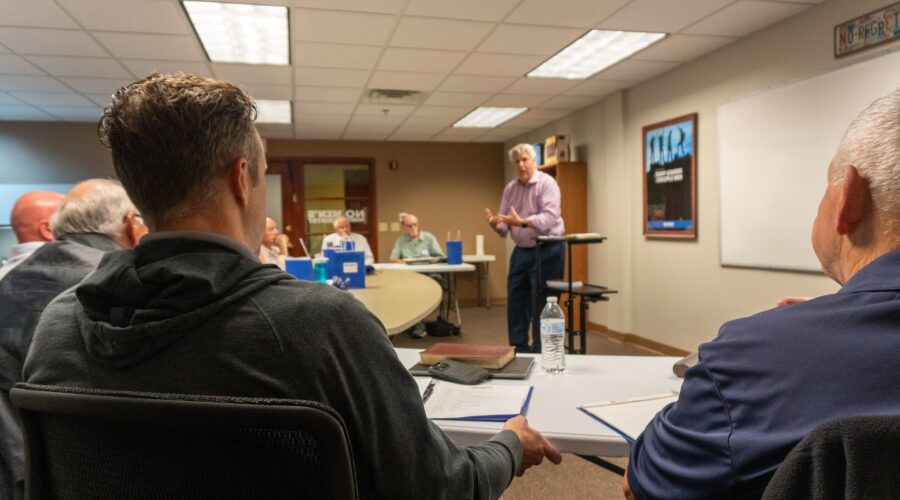 Man speaking to a group of other men gathered around the table
