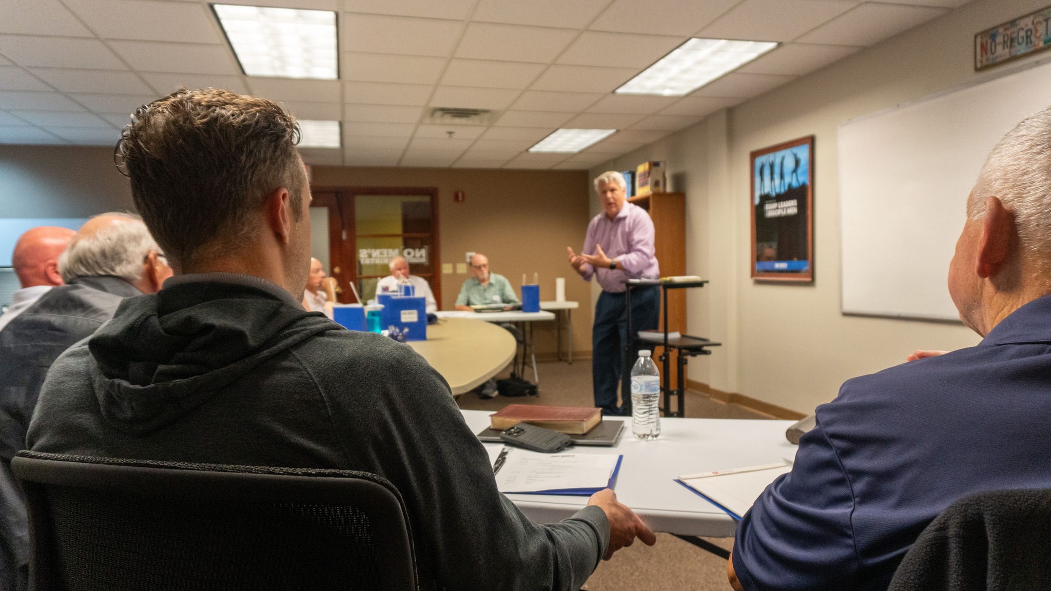 Man speaking to a group of other men gathered around the table