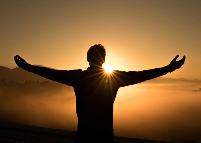 man looking at a sunrise with open arms