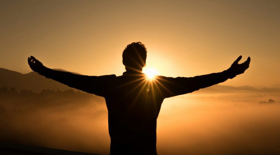 man looking at a sunrise with open arms