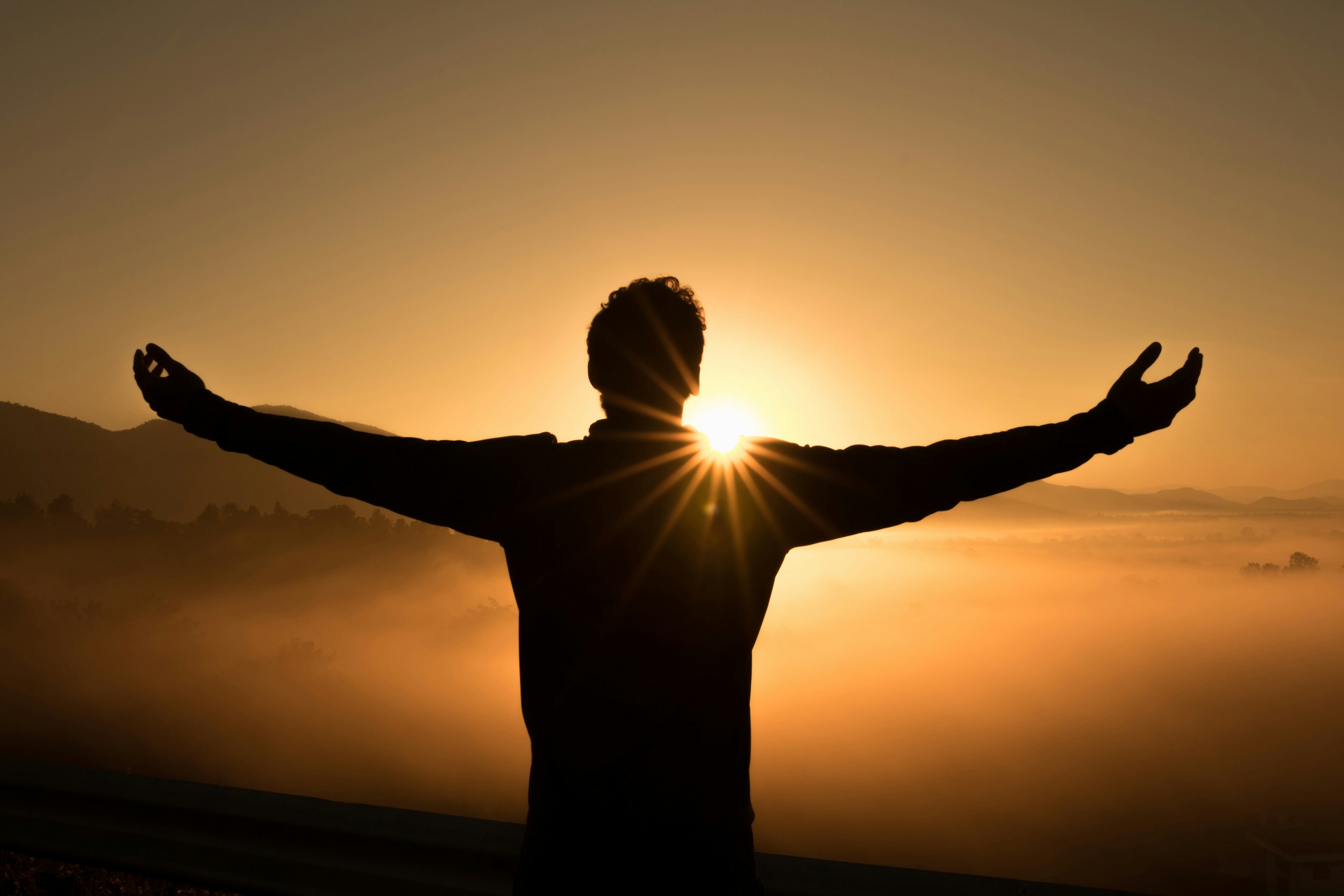 man looking at a sunrise with open arms