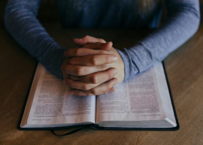 man-praying folded hands over a Bible