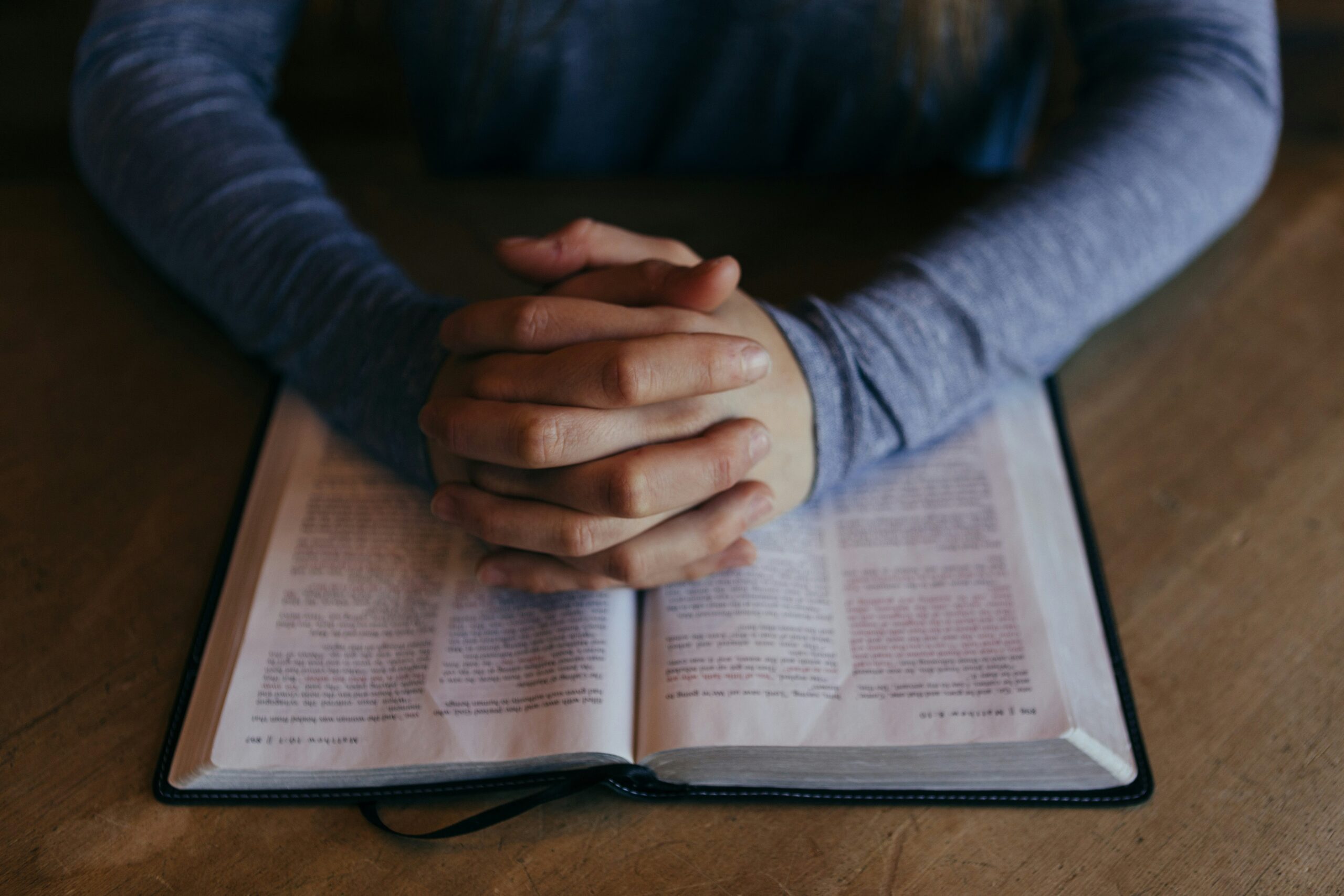 folded hands over a Bible